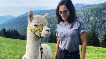 Ragazza con lama in montagna Ragazza accanto a una lama su un prato con vista sulle montagne.